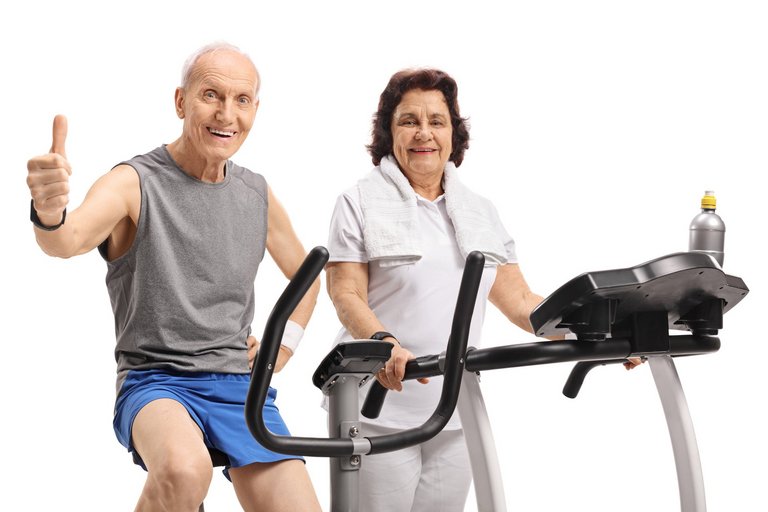 Elderly man on an exercise bike making a thumb up sign with an elderly woman on a treadmill